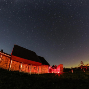 Battlesteads Dark Sky Observatory is illuminated in red light at night. Stars stud the deep blue sky above it.