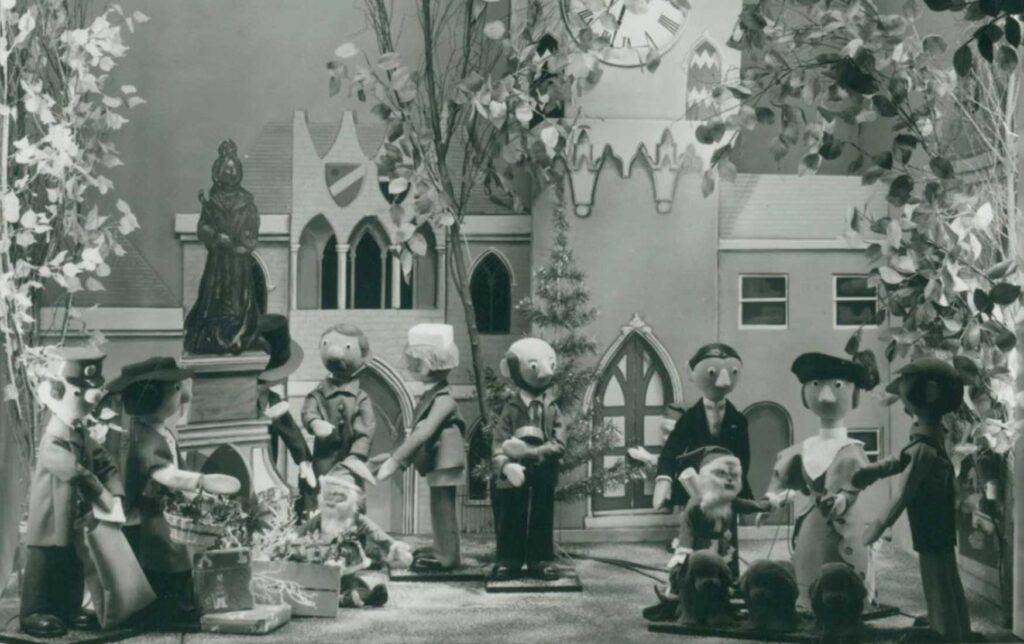 Characters from the TV show Camberwick Green stand in the Fenwick Window Display. They cluster outside a model of a festive church. This was the first Fenwick window display in 1971.