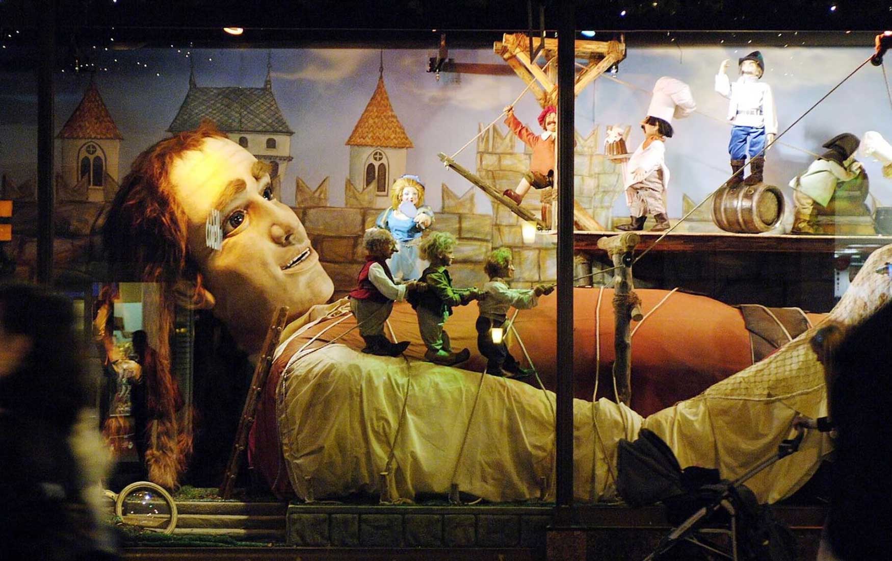 A huge figurine of a giant man lying down fills the Fenwick window display. Tiny figurines stand on top of him. This was a Gulliver's Travels themed window display at Fenwick Newcastle in 2006.