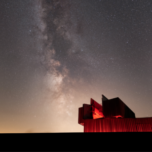 Kielder Observatory is illuminated in red light. It sits beneath a vast starry sky.