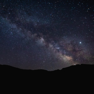 The black outlines of hills can be seen against a dark, purple blue sky covered with stars. 