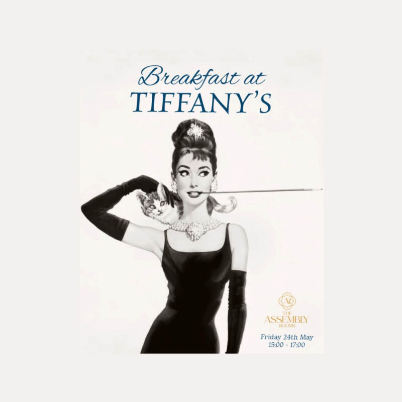 Black and white depiction of Audrey Hepburn in Breakfast at Tiffany's. She wears a sleek black dress, long black gloves and a high bun.
