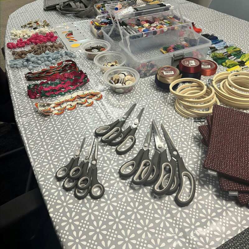 A table is covered in piles of scissors, buttons, threads, embellishments and more for the cushion decorating workshop at Banyan.