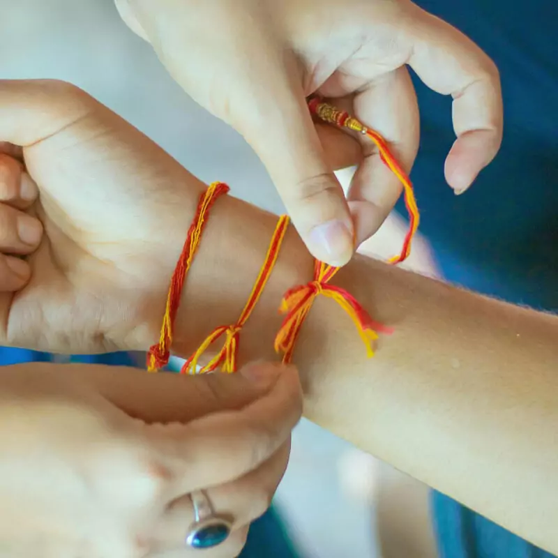 A person ties a red and orange friendship bracelet around the wrist of their friend.
