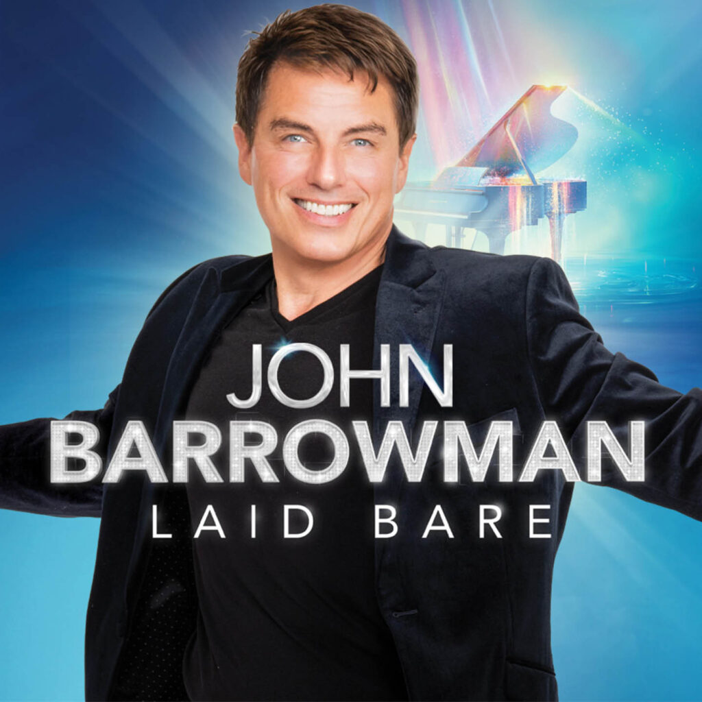 John Barrowman stands against a blue background with a piano illuminated in rainbow light. He stands with his arms spread grandly. White sparkly text overlays the image. It says: John Barrowman Laid Bare.
