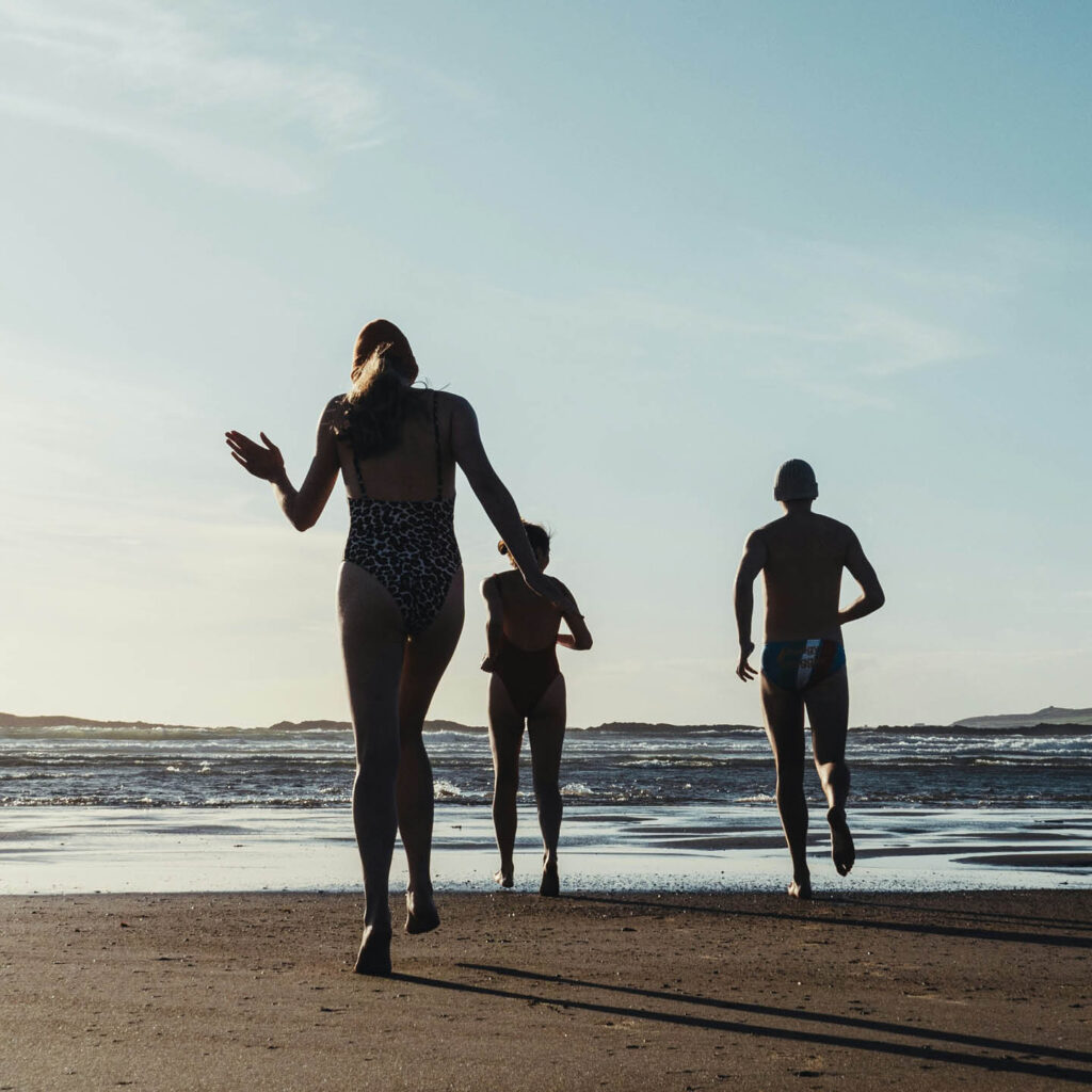 Three people run across the sand towards the open sea.