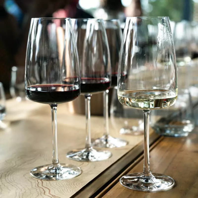 Three glasses of wine are clustered together on a table. Two of them are filled with a small amount of red wine, while the other contains white wine.