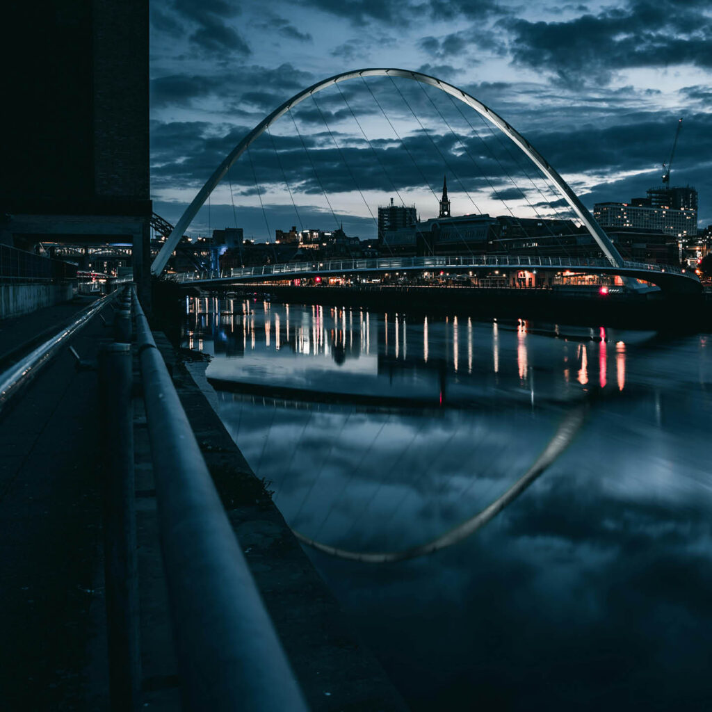 Dark, stormy rain clouds gather above Newcastle's Millenium Bridge and the quayside. The water reflects the clouds eerily.