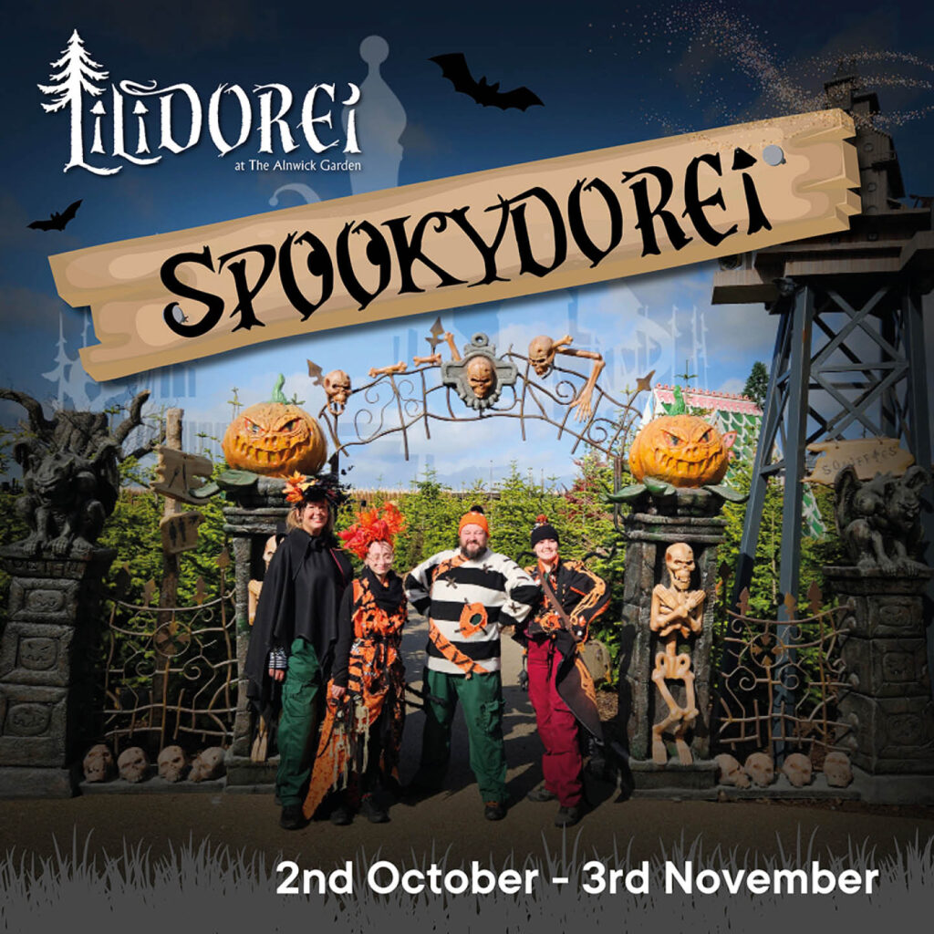 Team members at The Alnwick Garden dressed up in pumpkin style Halloween costumes. They smile and stand in front of the entrance to Lilidorei. A wooden plank overlays the image, carved with the word Spookydorei.