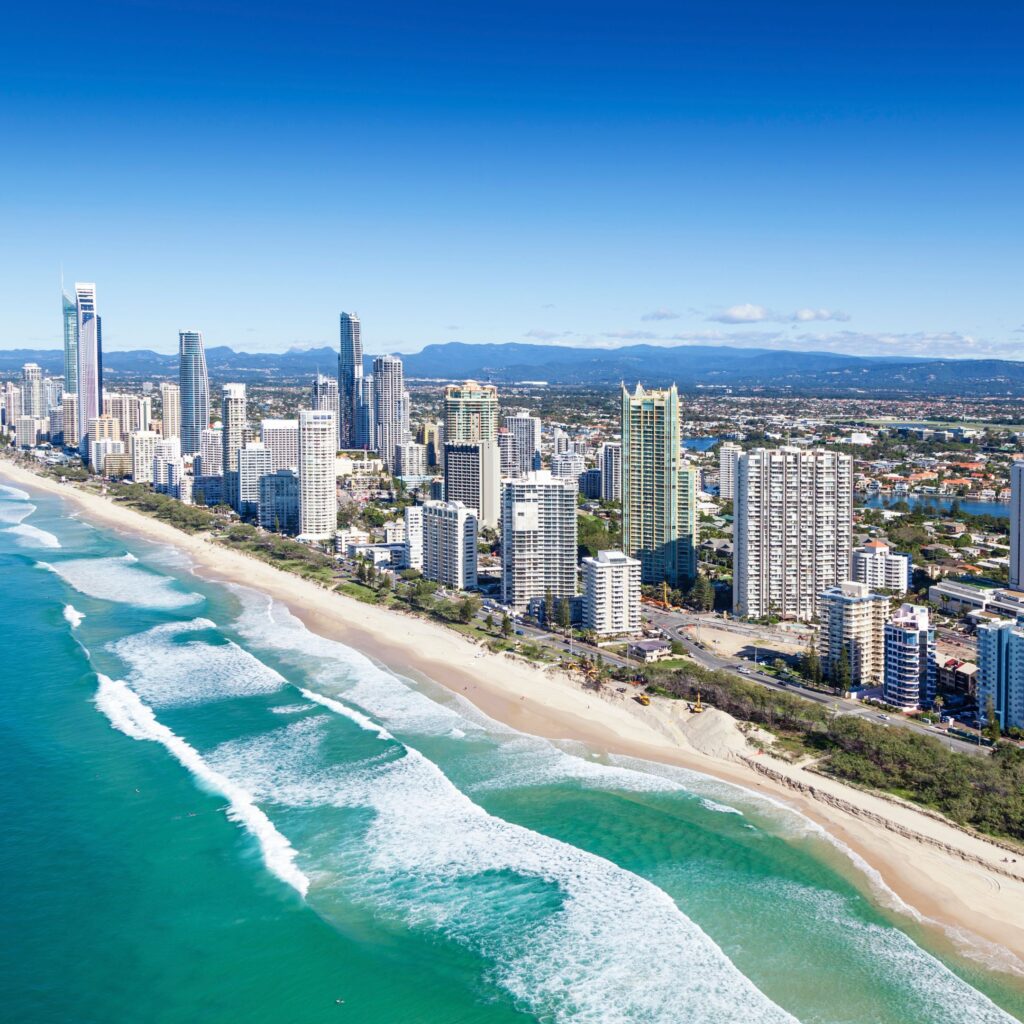An overhead image of the blue sky and blue water of Australia is broken up by the city, a line of skycrapers and tall buildings