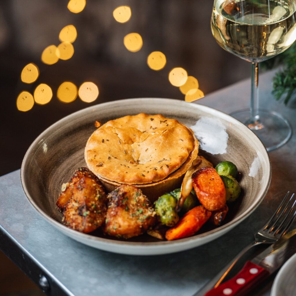 A plate of vegetables and a festive pie are served in a cosy atmosphere