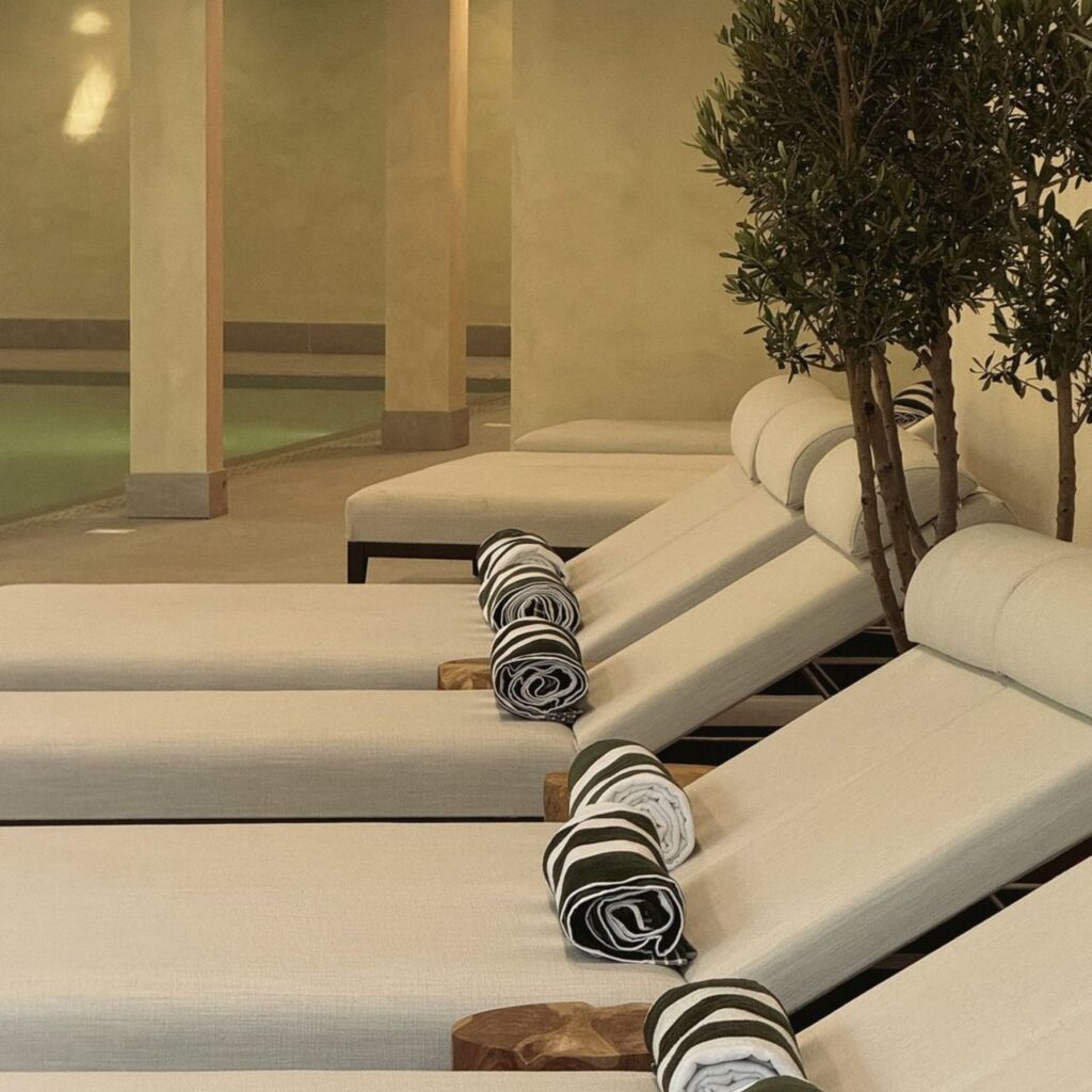 Next to a pool, white comfy lounge chairs are all lined up ready to be used with a towel neatly folder on each seat.
