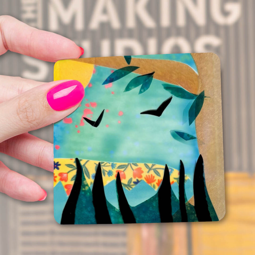 A person holds up a coaster depicting a tree and flying birds.