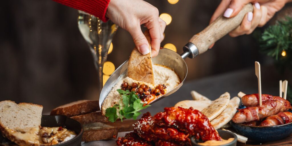 A large spread of mouthwatering appetisers featuring creamy humus, korean fried chicken and baked Camembert
