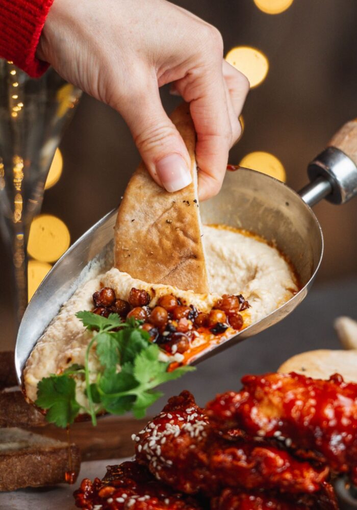 A large spread of mouthwatering appetisers featuring creamy humus, korean fried chicken and baked Camembert