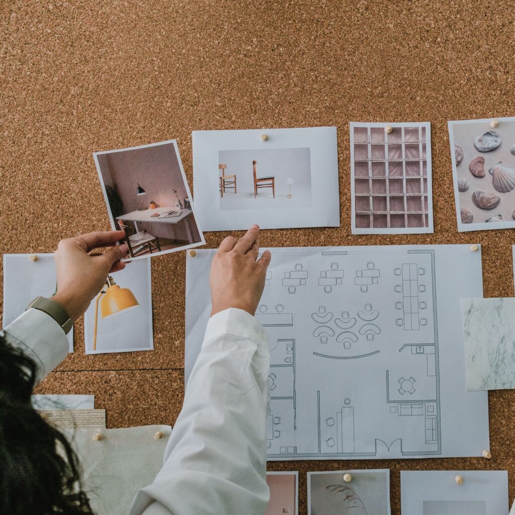A woman reaches up to pin a photo to her vision board that is mounted on the wall. The images feature aesthetic images and drawings of plans she has.