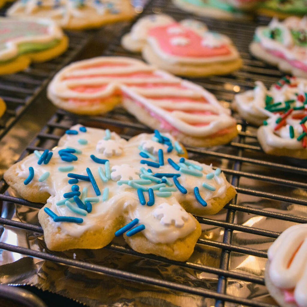 Biscuits shaped like snowflakes, candy canes and stockings sit on a baking tray. They are decorated with different coloured icing and sprinkles.