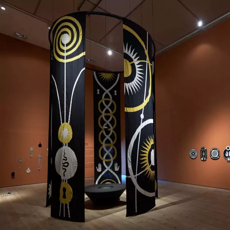Large black banners featuring white and yellow totemic symbols hang from the ceiling to the floor in one of the Baltic's large exhibition spaces. This is part of the Mani Kambo exhibition.