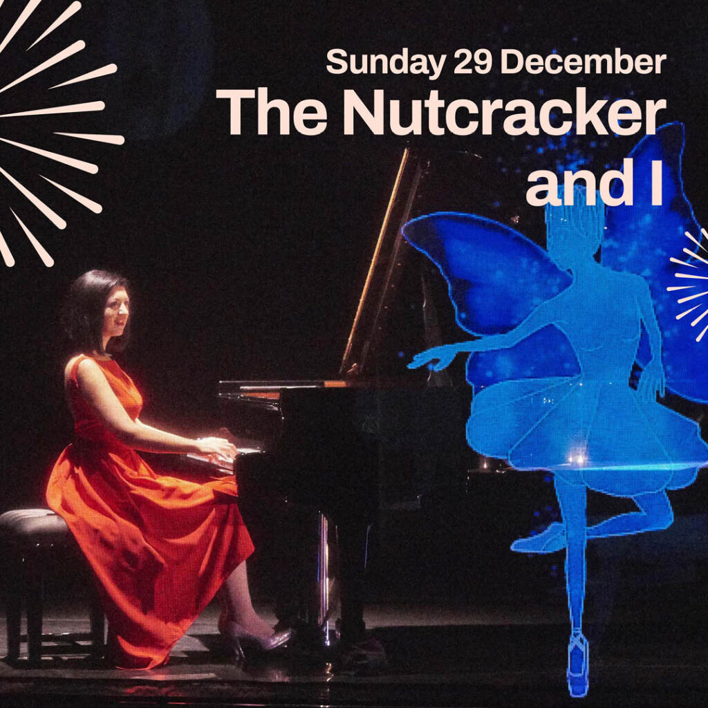 A pianist in a long red dress plays a black piano on a dimly lit stage. She smiles and watches a blue projection of a fairy dance across the stage.