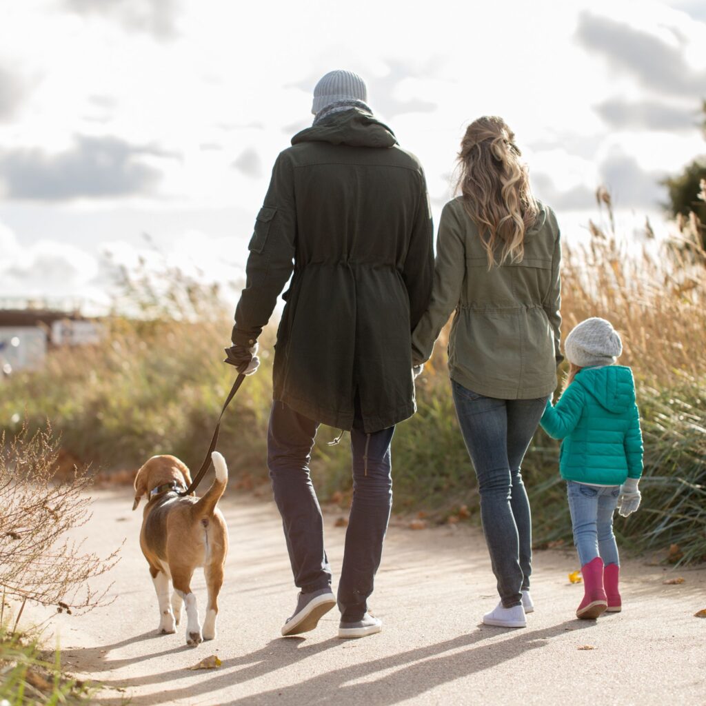 A family takes a walk with their dog in the winter sun