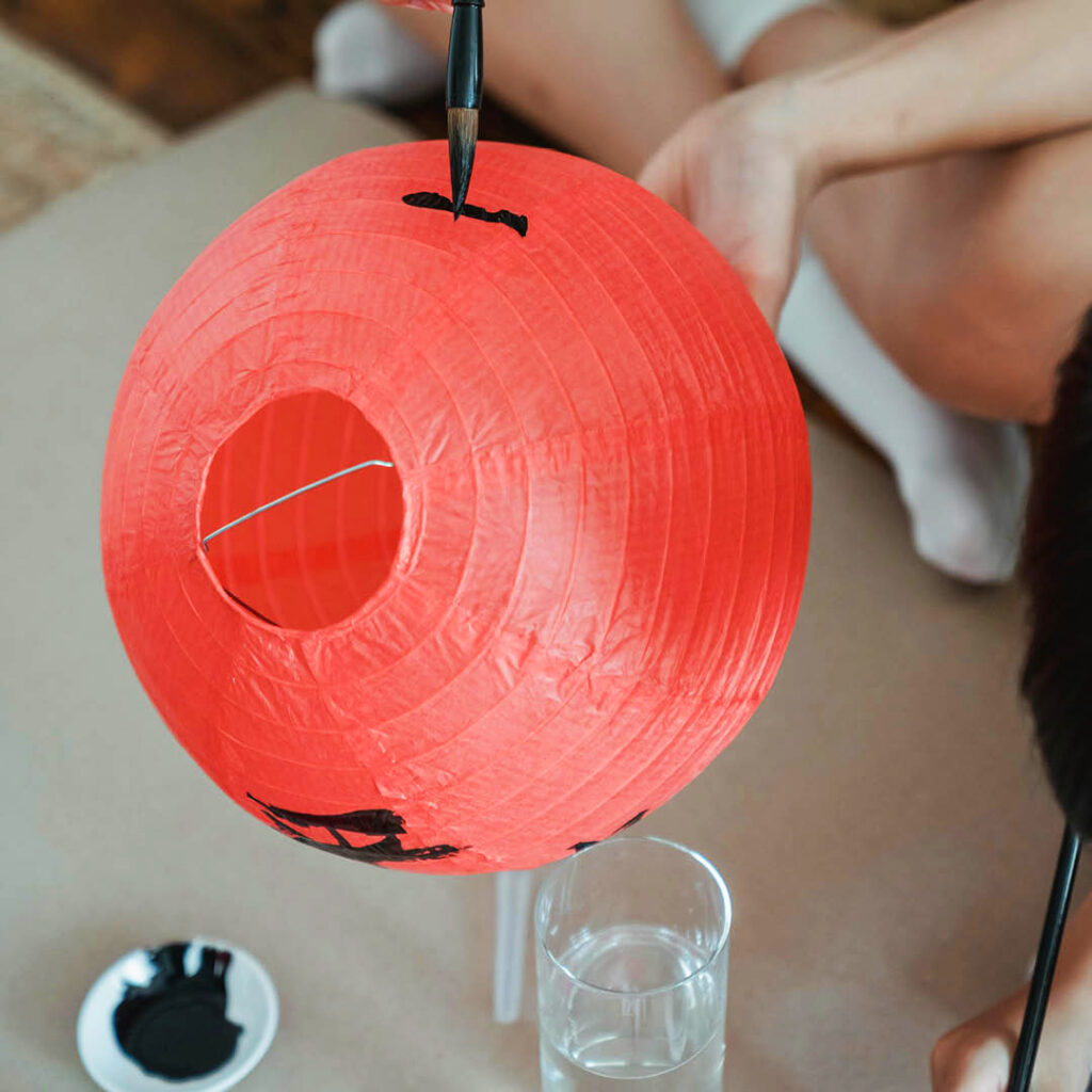 An unseen person paints a black symbol on a red paper lantern for Lunar New Year.