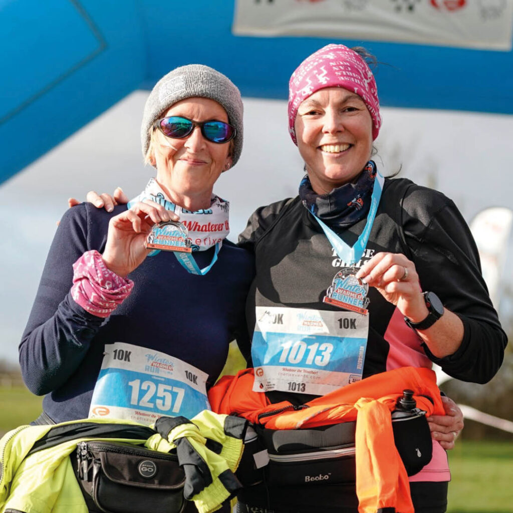 Two women in running gear and winter hats grin at the camera as they hold up their Newcastle 10k run medals.
