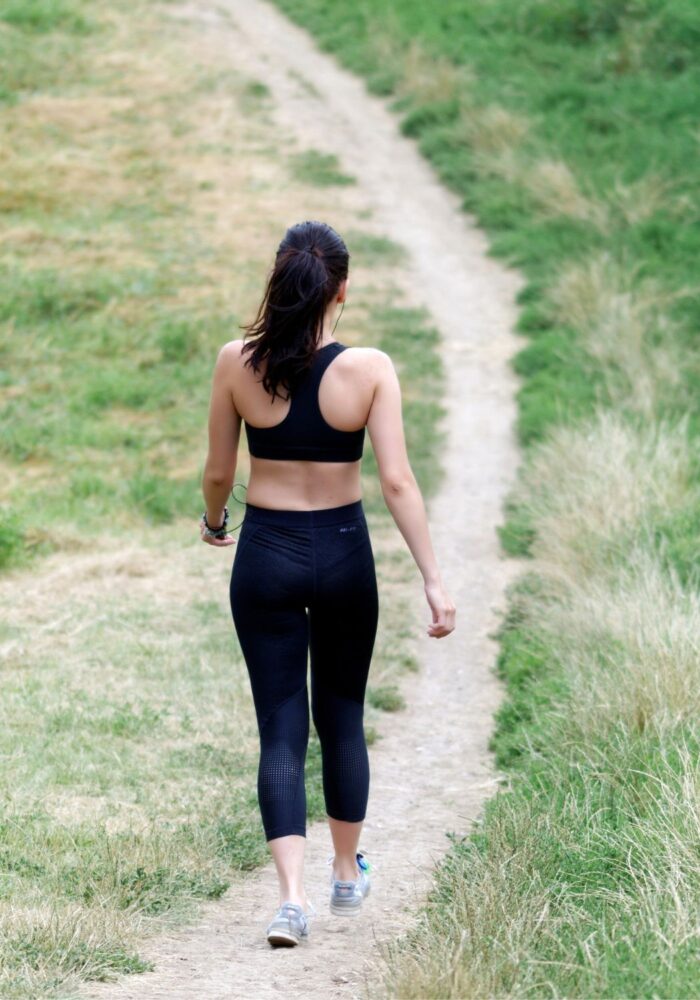 A girl in a black workout set walks along a green path