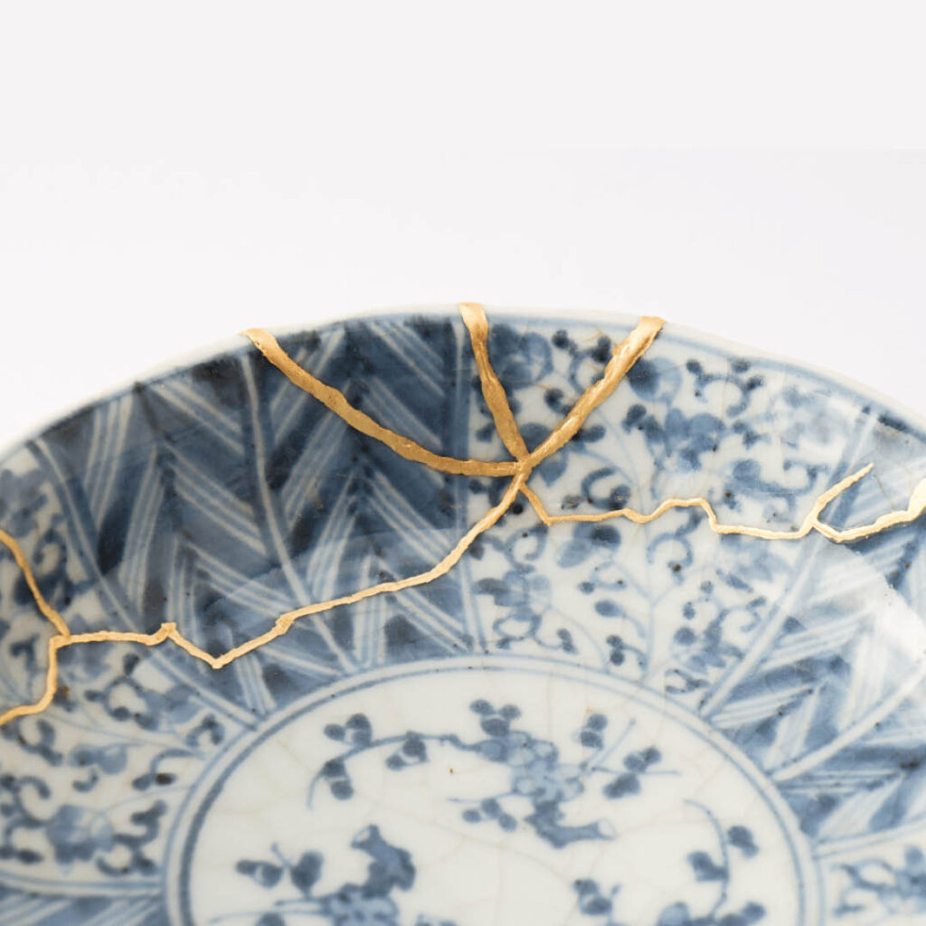 A blue and white plate has been pieced back together using the kintsugi method. The cracks are filled with gold paint.