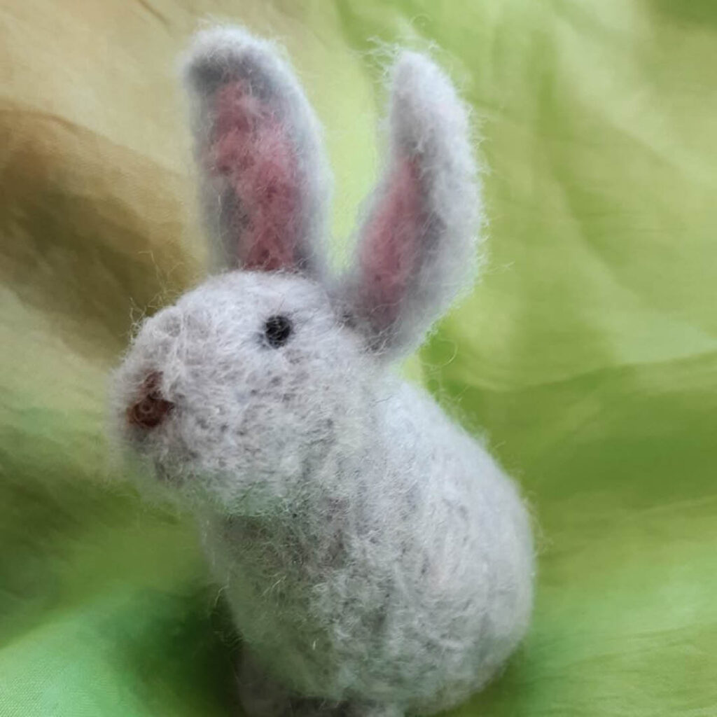 A cute grey felted bunny with pink ears and small black eyes. It has been made during a needle felting workshop.