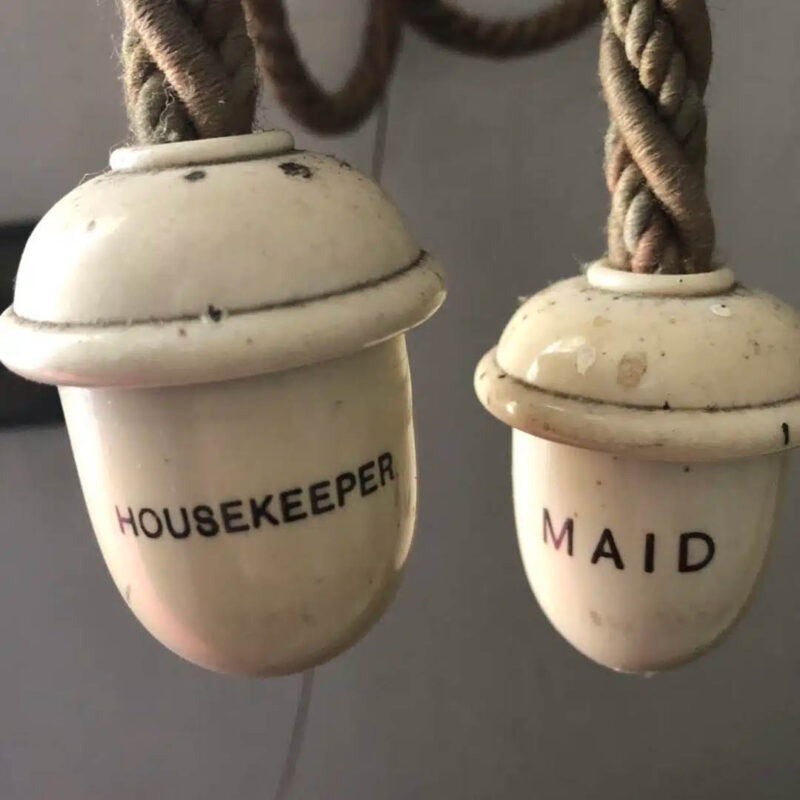 Two white bells hang from thick ropes. One has the words Housekeeper painted onto it. The other features the word Maid.