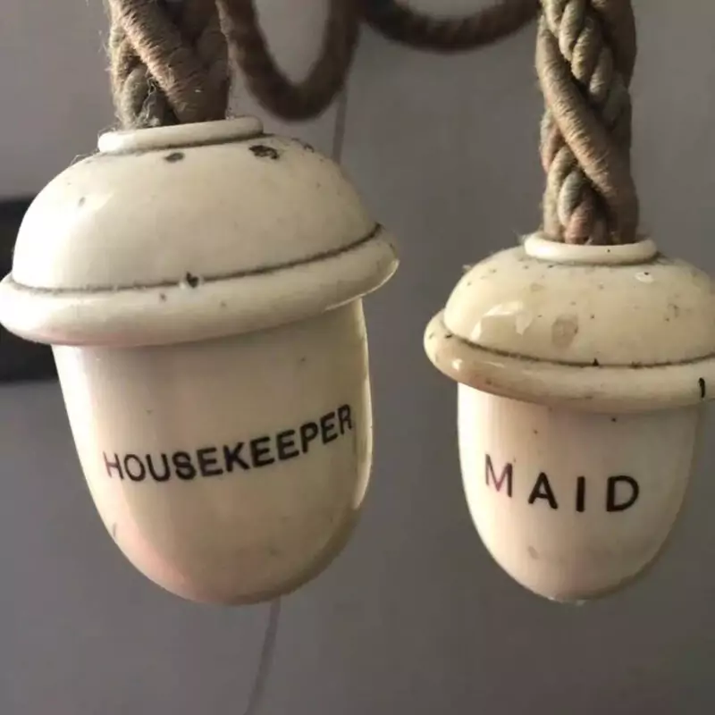 Two white bells hang from thick ropes. One has the words Housekeeper painted onto it. The other features the word Maid.
