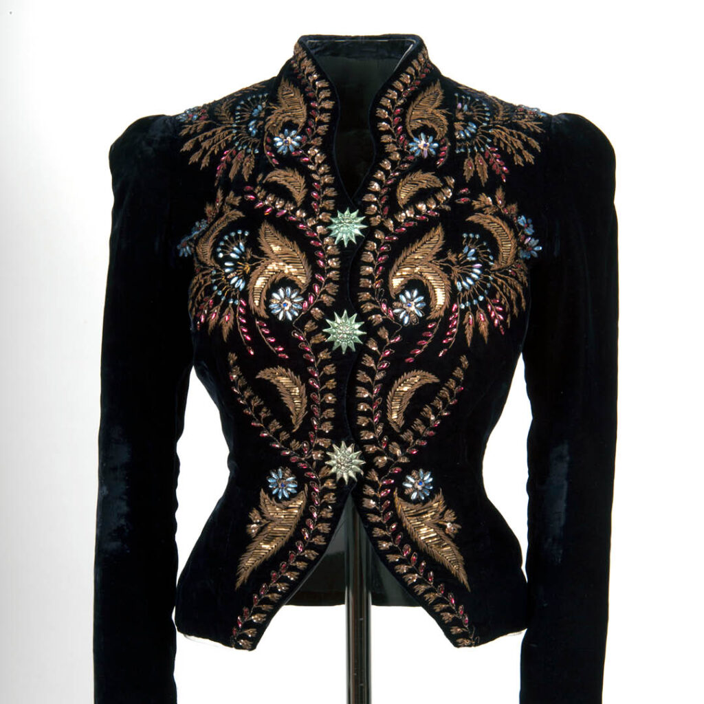 A black velvet coat embroidered with beautiful swirling gold patterns and blue gemstone embellishments.