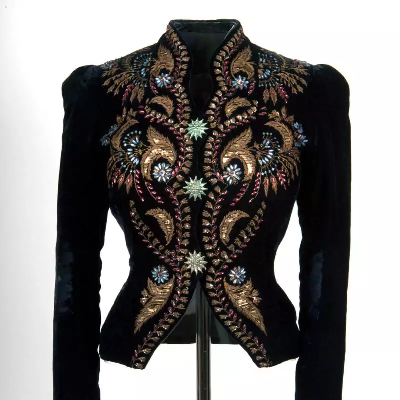 A black velvet coat embroidered with beautiful swirling gold patterns and blue gemstone embellishments.