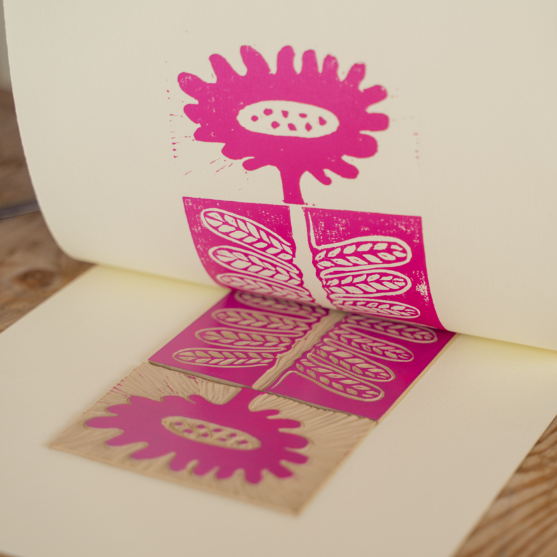 A pink flower design has been lino printed onto a sheet of paper in bright pink paint.
