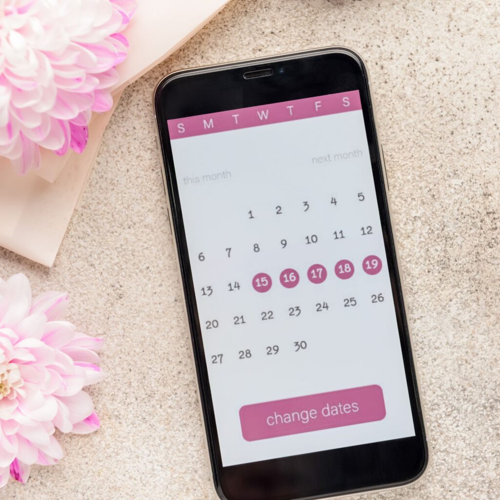 On the table a woman's phone displays her current menstral cycle on a calendar