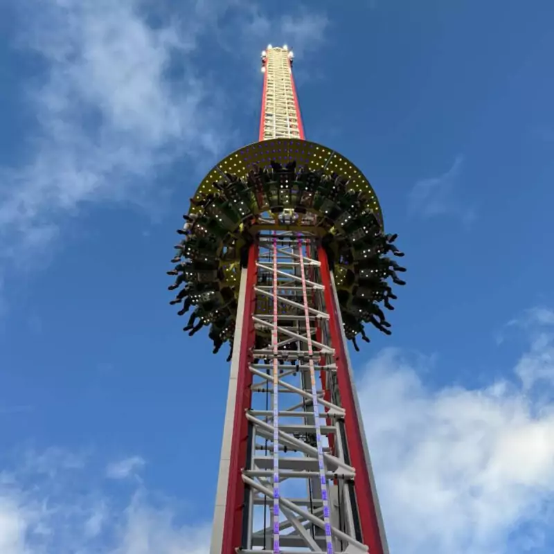 The Drop Tower ride stands against a bright blue sky. People's legs dangle from the seats encircling the middle tower. This is one of the rides at The Hopping funfair this summer.