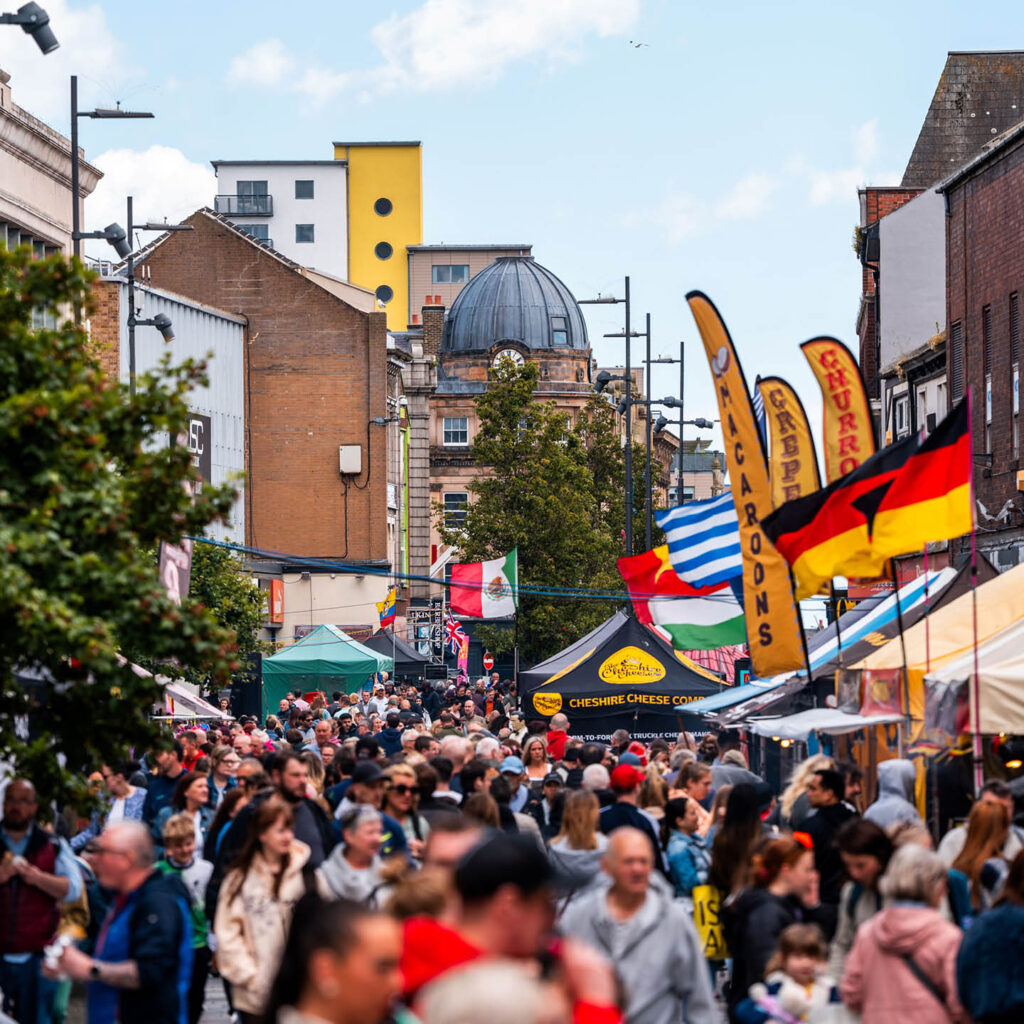 Swarms of people fill a street in Sunderland. Coloured gazebos and flags can be seen in the distance. They belong to the various food traders at Sunderland Food and Drink Festival.