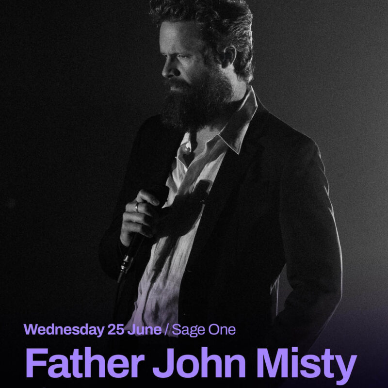 Father John Misty is a white man with dark hair and a beard. He wears a suit jacket over a shirt and holds his microphone to his chest, looking seriously ahead of him. He is cast completely in black and white light. Purple text overlays this image. It says: Father John Misty, Wednesday 25th June.