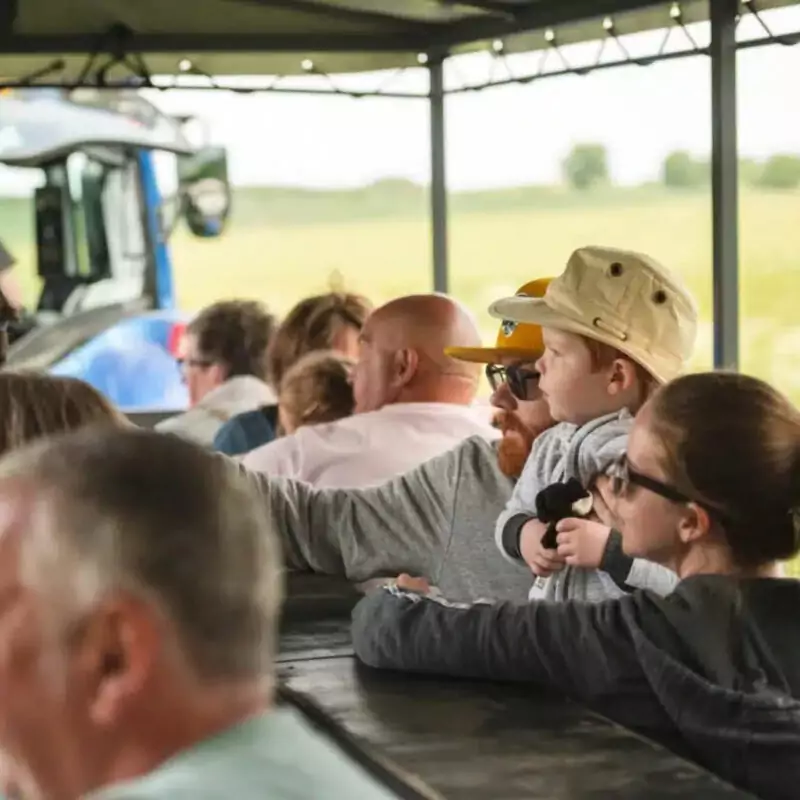 A father wearing a cap and sunglasses holds his son close to him. He points out something in the distant fields.