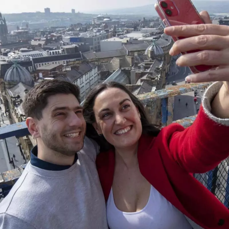 A couple grin as they take a selfie at the top of Greys Monument in Newcastle. Behind them, the city stretches into the distance.
