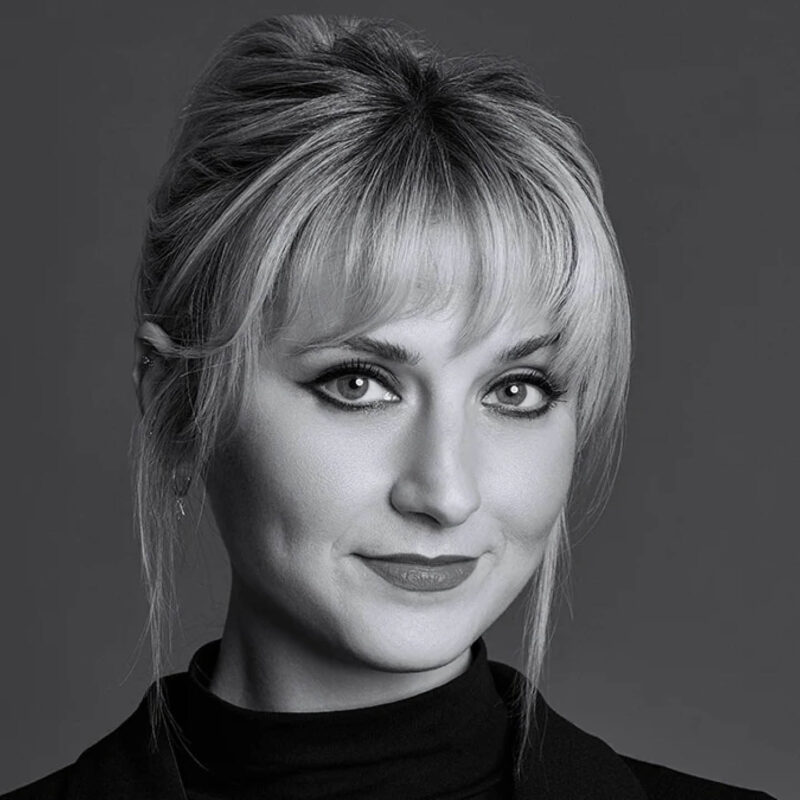 NARS makeup artist Jen Lyons smiles at the camera. Her blond hair is pulled up and she wears dark smokey eyed makeup.