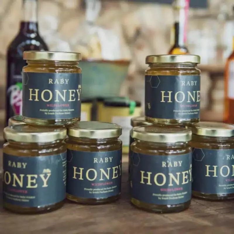 Stacked jars of Raby Honey on a wooden surface.