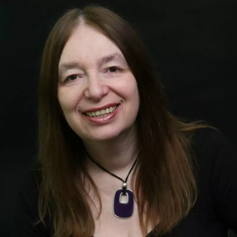 Alison Weir is a white woman with long brown hair. She smiles at the camera against a black background.