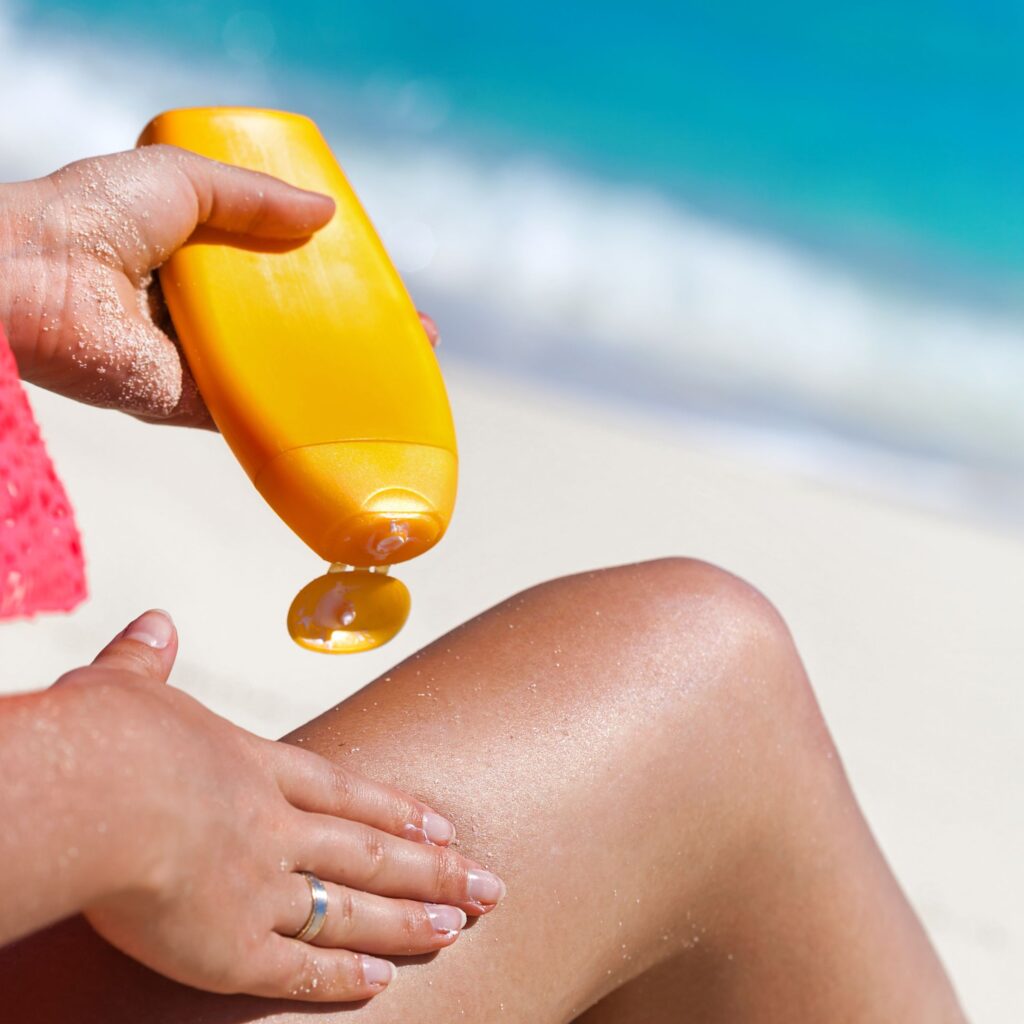 A woman applies SPF sun tan lotion on her leg on the beach