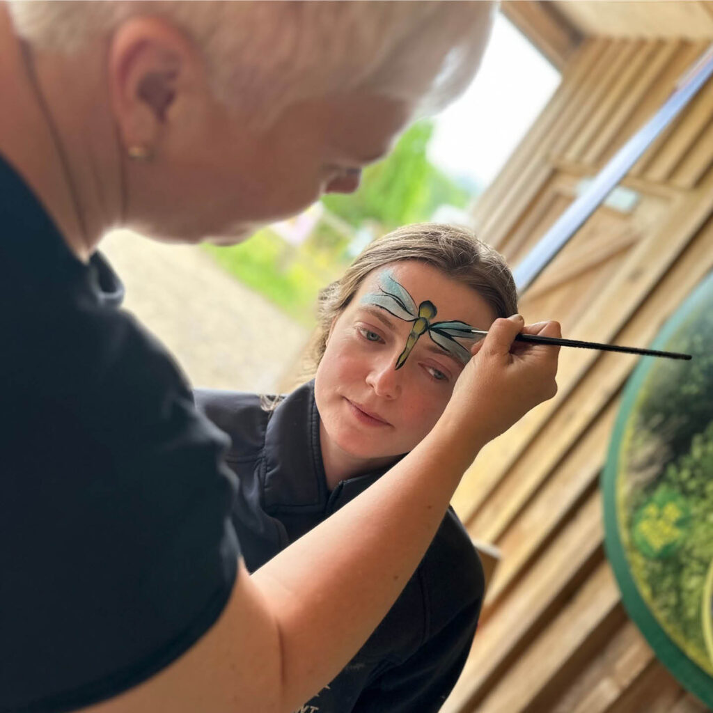 A woman paints a blue dragonfly onto the forehead of a young woman for the Dragonfly Family Fun Day at Washington Wetland Centre.